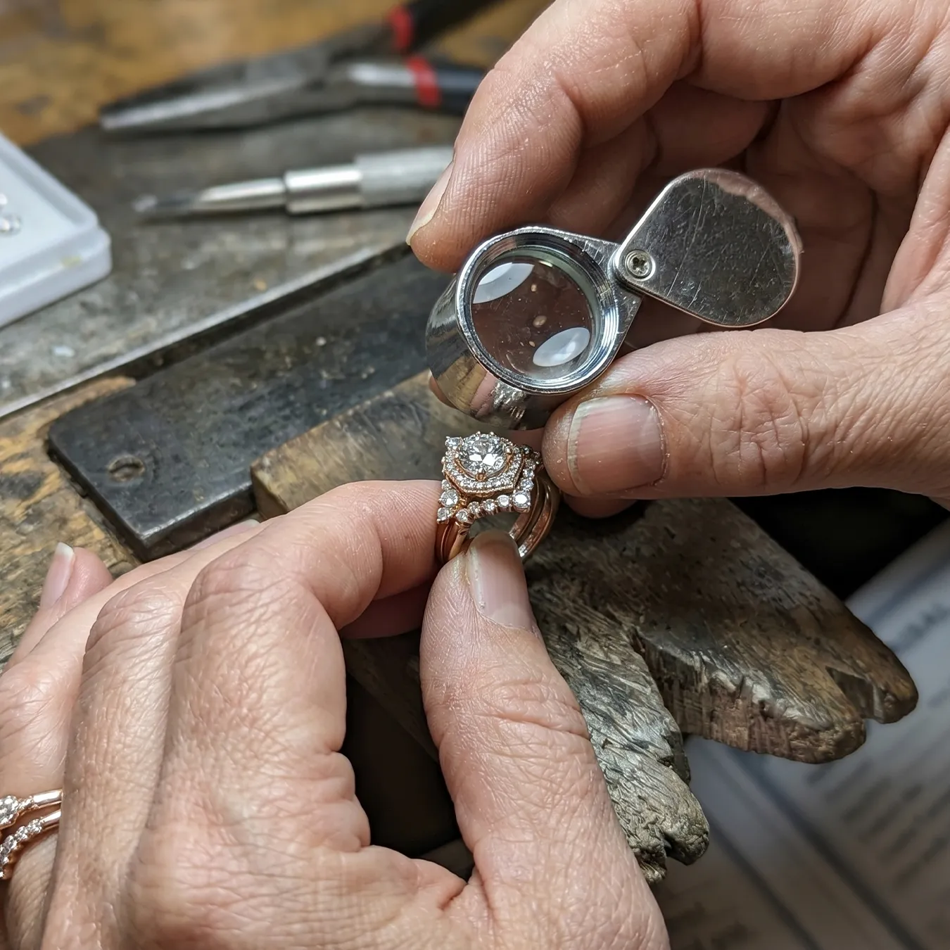 A jeweler inspects a diamond ring with a magnifying loupe on a workbench.