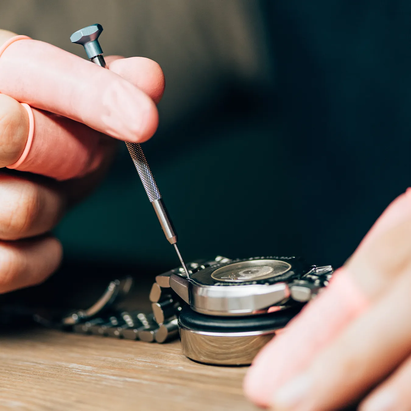 Watchmaker using a precision tool to repair a watch on a wooden table.