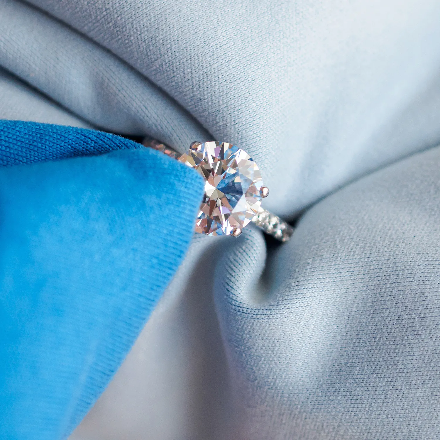 A diamond ring being polished with a blue cloth on a light fabric background.