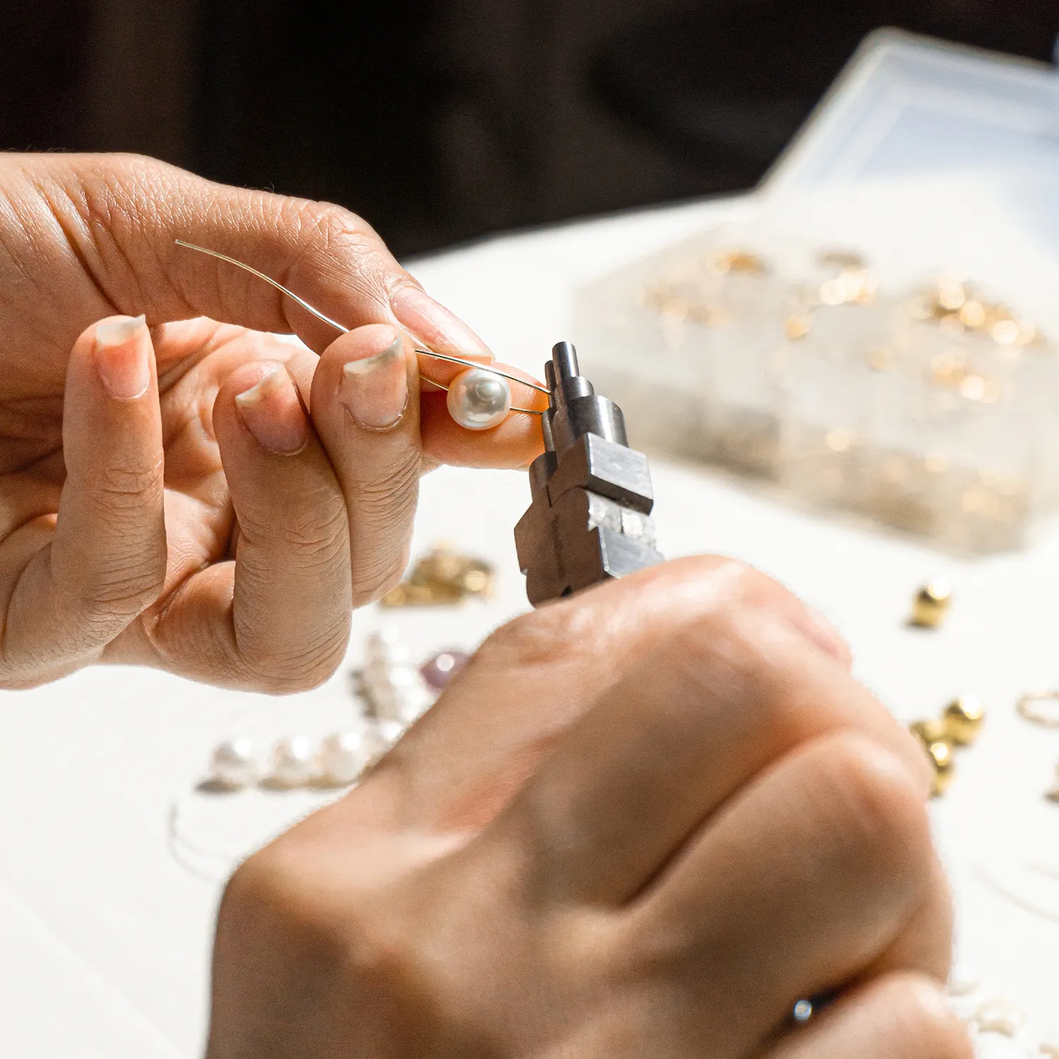 Jeweler using pliers to adjust a pearl on a wire at a workbench.