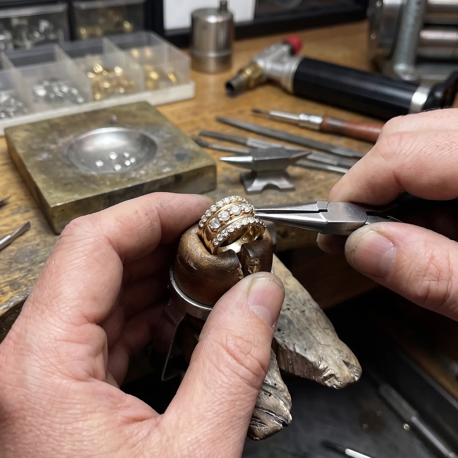 Jeweler using pliers to adjust a diamond ring on a workbench.