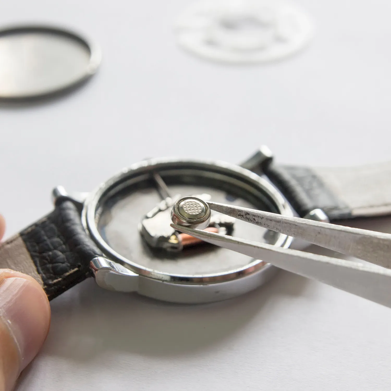 Watch battery being replaced with tweezers, showcasing intricate watch repair.