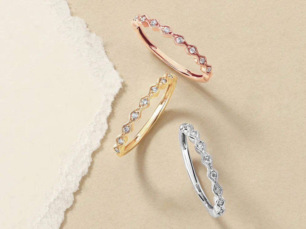 Three elegant diamond rings in rose gold, yellow gold, and silver, displayed on a beige background.