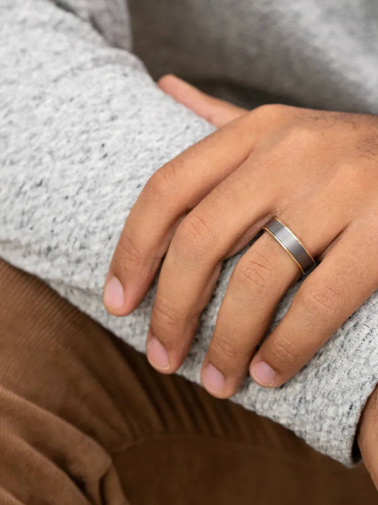 Close-up of a hand wearing a sleek two-tone ring, resting on a gray sweater.