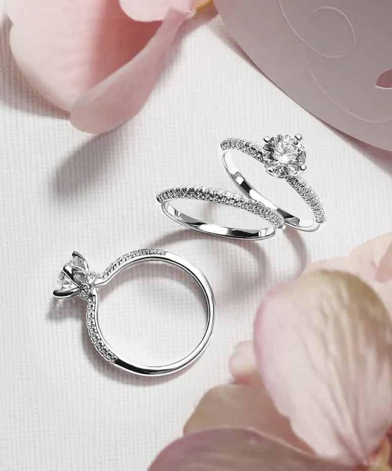 Three elegant diamond engagement rings displayed with soft pink petals in the background.