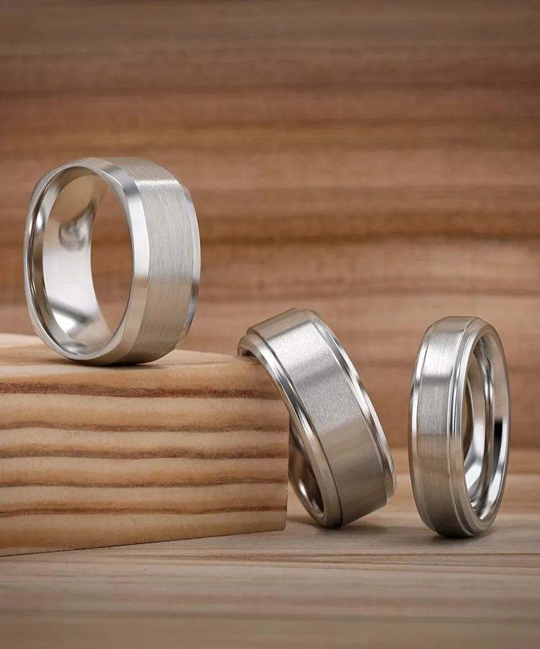 Three elegant wedding bands displayed on wood, showcasing a mix of finishes and styles.