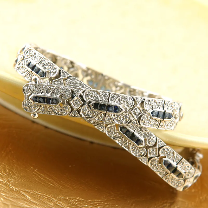 Elegant silver bracelet with intricate design and blue gemstones, displayed on a golden surface.