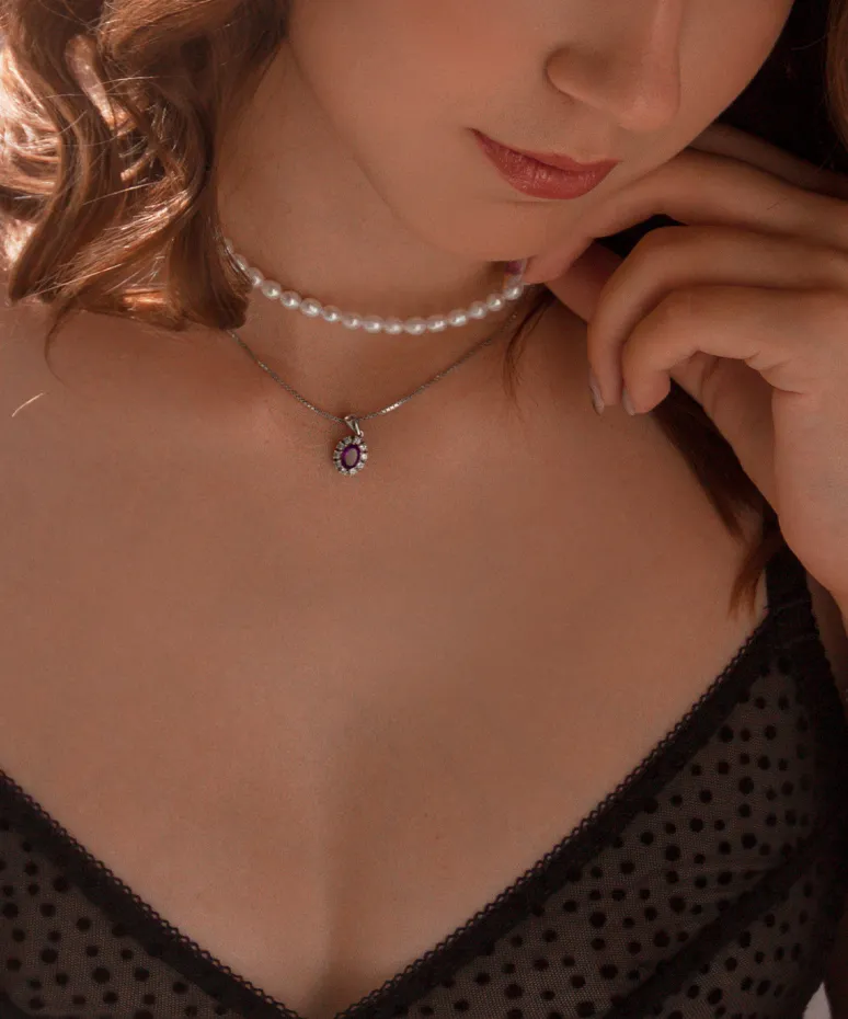 Close-up of a woman wearing a pearl choker and a silver necklace with a purple gemstone pendant.