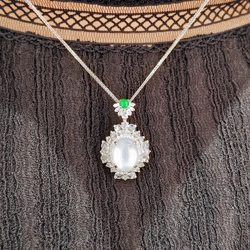 Elegant silver necklace with a large oval stone and green accent, displayed on textured black fabric. Shop at Genesis Jewelry.