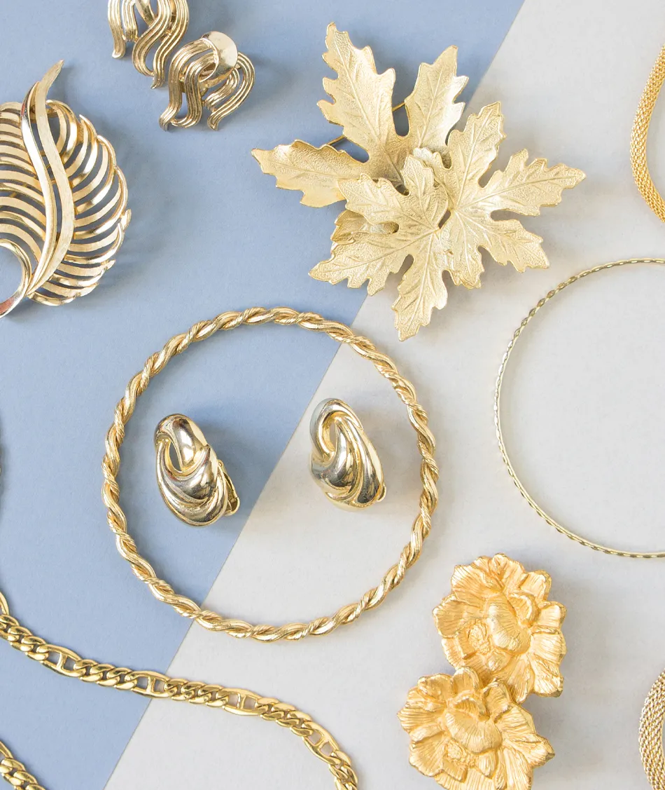 Gold jewelry pieces including earrings, brooches, and chains arranged on a blue and white background.