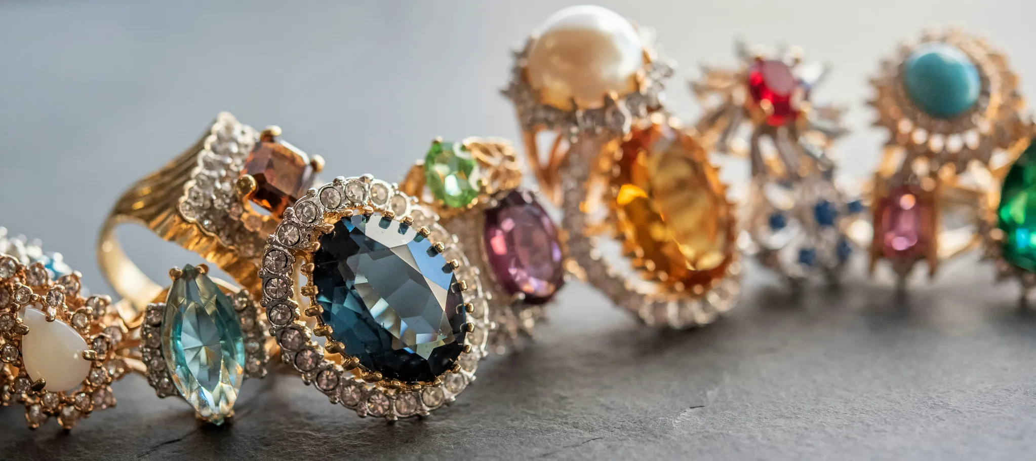 Colorful gemstone rings with intricate designs displayed on a dark surface.