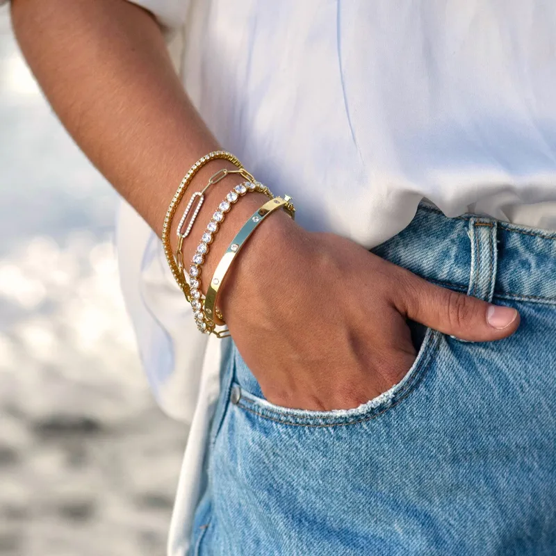 Close-up of a hand wearing multiple stylish bracelets, showcasing gold and crystal designs.