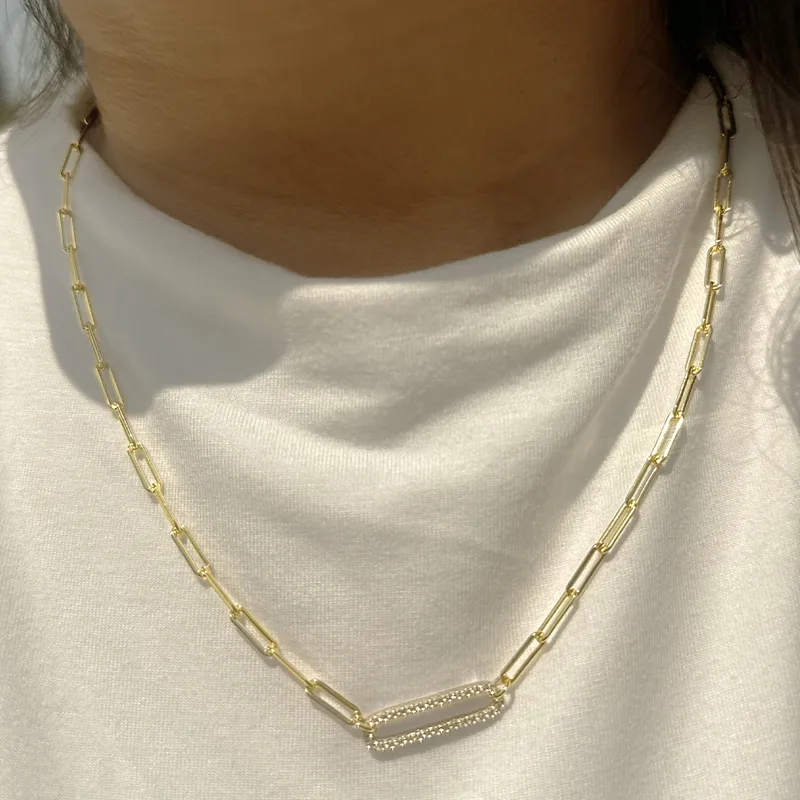 Gold chain necklace with a unique link design, worn on a person in a white shirt.
