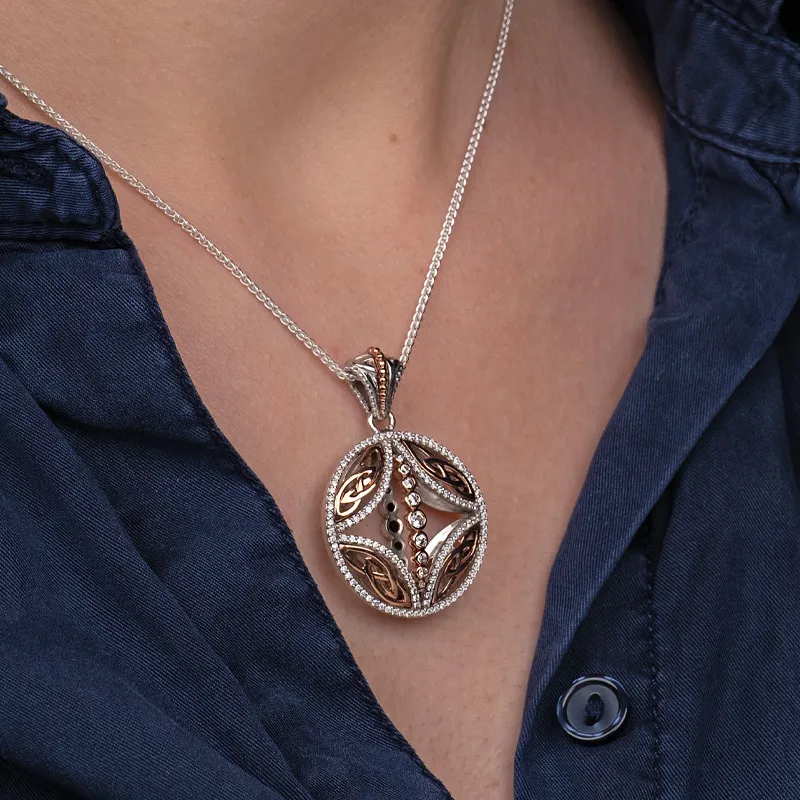 Elegant silver and rose gold pendant necklace with intricate design, worn on a dark shirt.