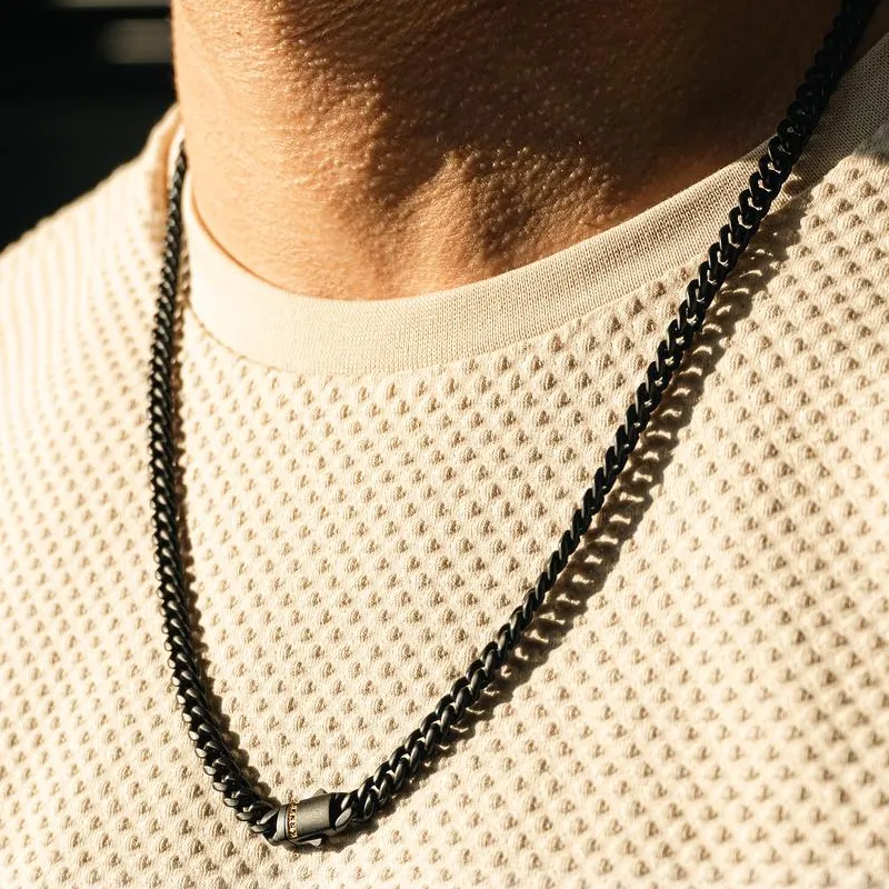Close-up of a black chain necklace worn over a textured cream shirt, showcasing its design and shine.