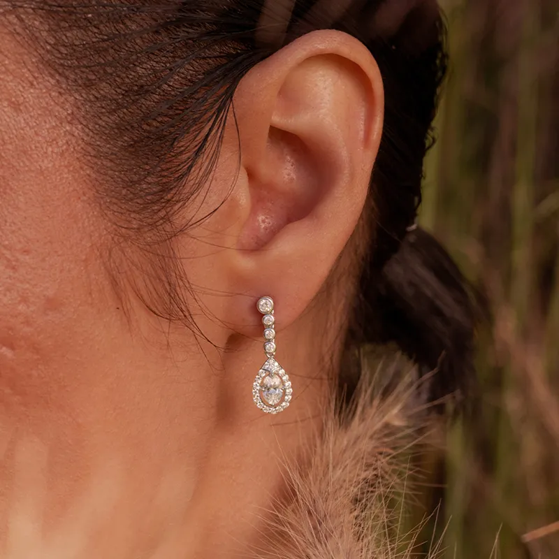 Elegant drop earrings with sparkling diamonds, showcased on a model's ear.