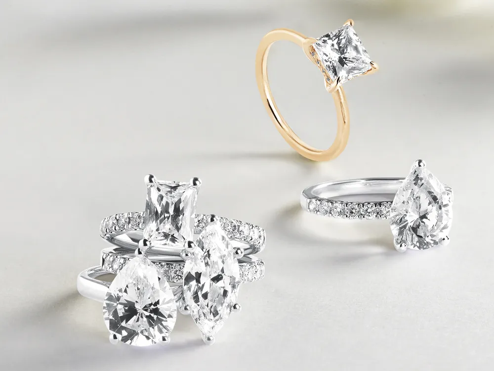 Elegant collection of diamond rings featuring various cuts, including pear and princess, displayed on a light background.