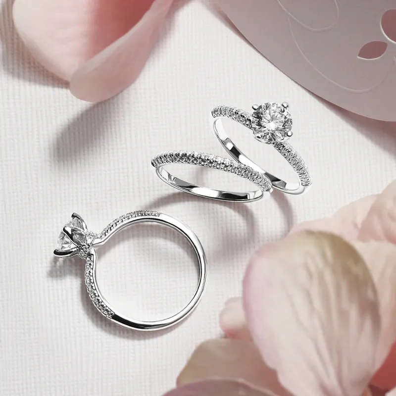 Three elegant silver engagement rings with diamonds, surrounded by soft pink petals.