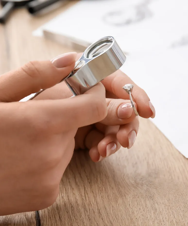 A person examining a diamond ring with a magnifying glass on a wooden surface at Genesis Jewelry in Muscle Shoals.