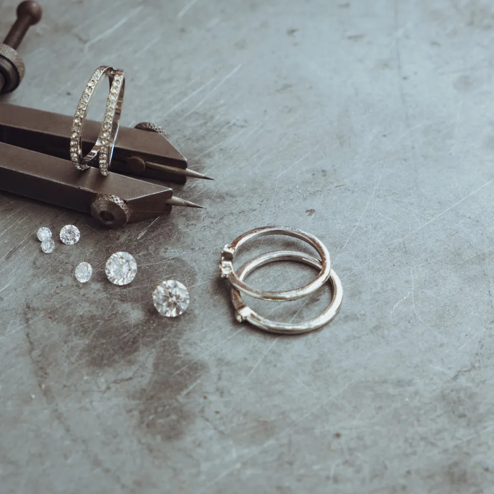 Jewelry tools and diamond rings on a metal surface, showcasing fine jewelry craftsmanship at Genesis Jewelry, Muscle Shoals.