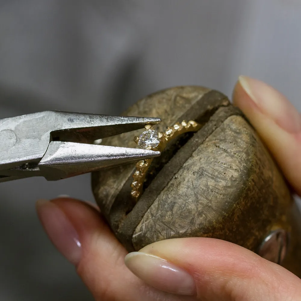 Jeweler using pliers to set a diamond in a gold ring.