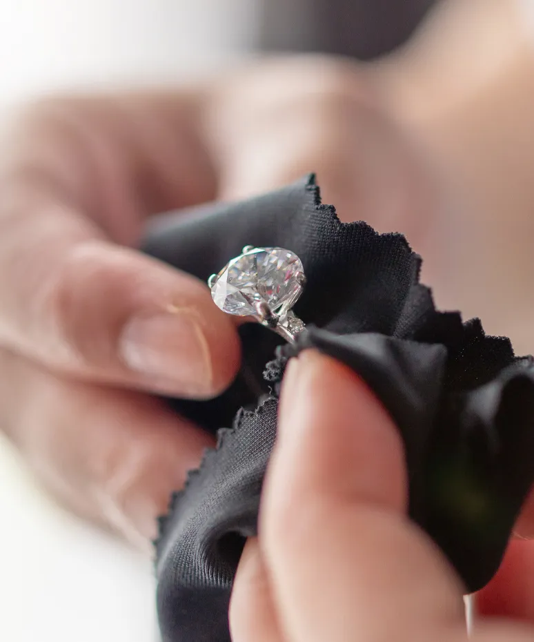 A person cleaning a diamond ring with a black cloth, showcasing jewelry care at Genesis Jewelry in Muscle Shoals.