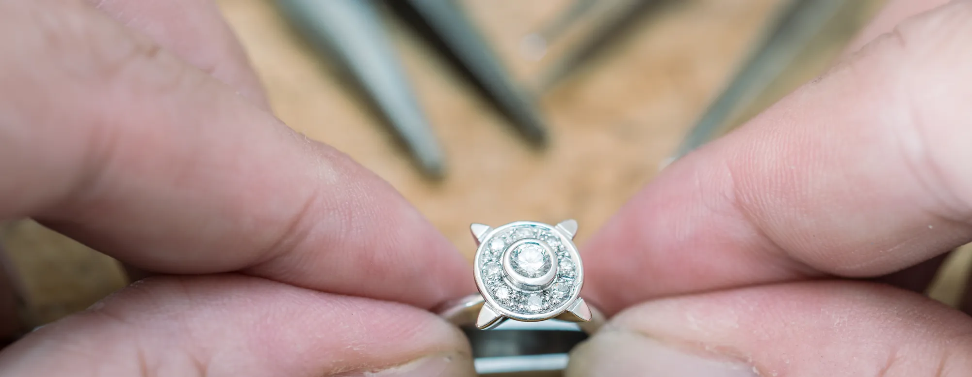Close-up of a diamond ring held between fingers, showcasing intricate design and sparkling stones.