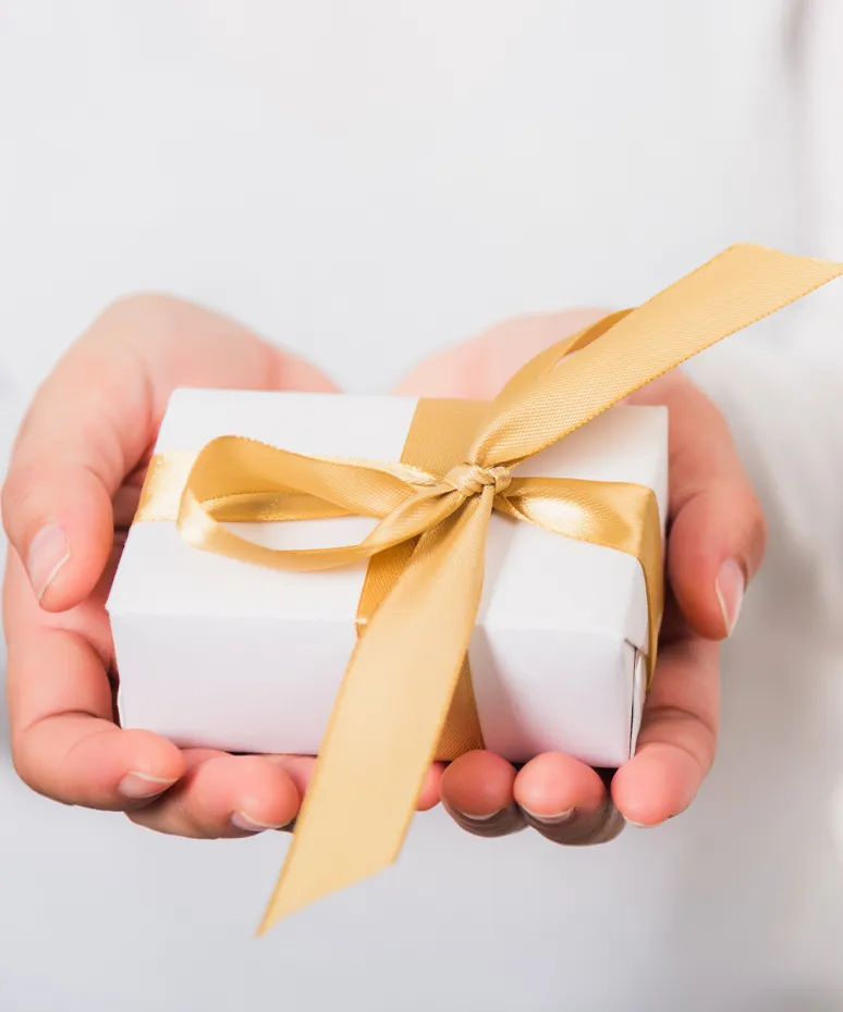 A person holding a small white gift box with a gold ribbon, symbolizing a present or special occasion.