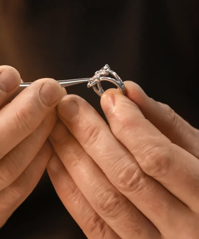 A jeweler carefully holds a silver engagement ring with a tool, showcasing craftsmanship.