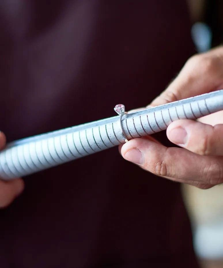 A jeweler holds a ring sizer with a diamond ring, showcasing the resizing process at Genesis Jewelry in Muscle Shoals.