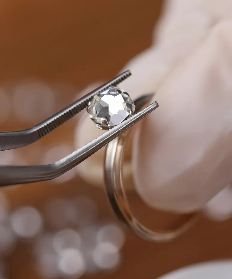 A jeweler using tweezers to hold a diamond above a ring, showcasing fine jewelry craftsmanship at Genesis Jewelry.