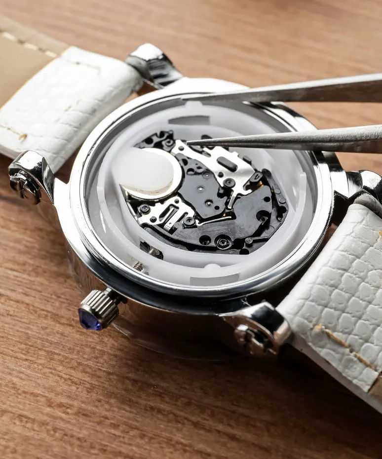 Close-up of a watch movement being repaired with tweezers, showcasing intricate mechanics inside the watch case.