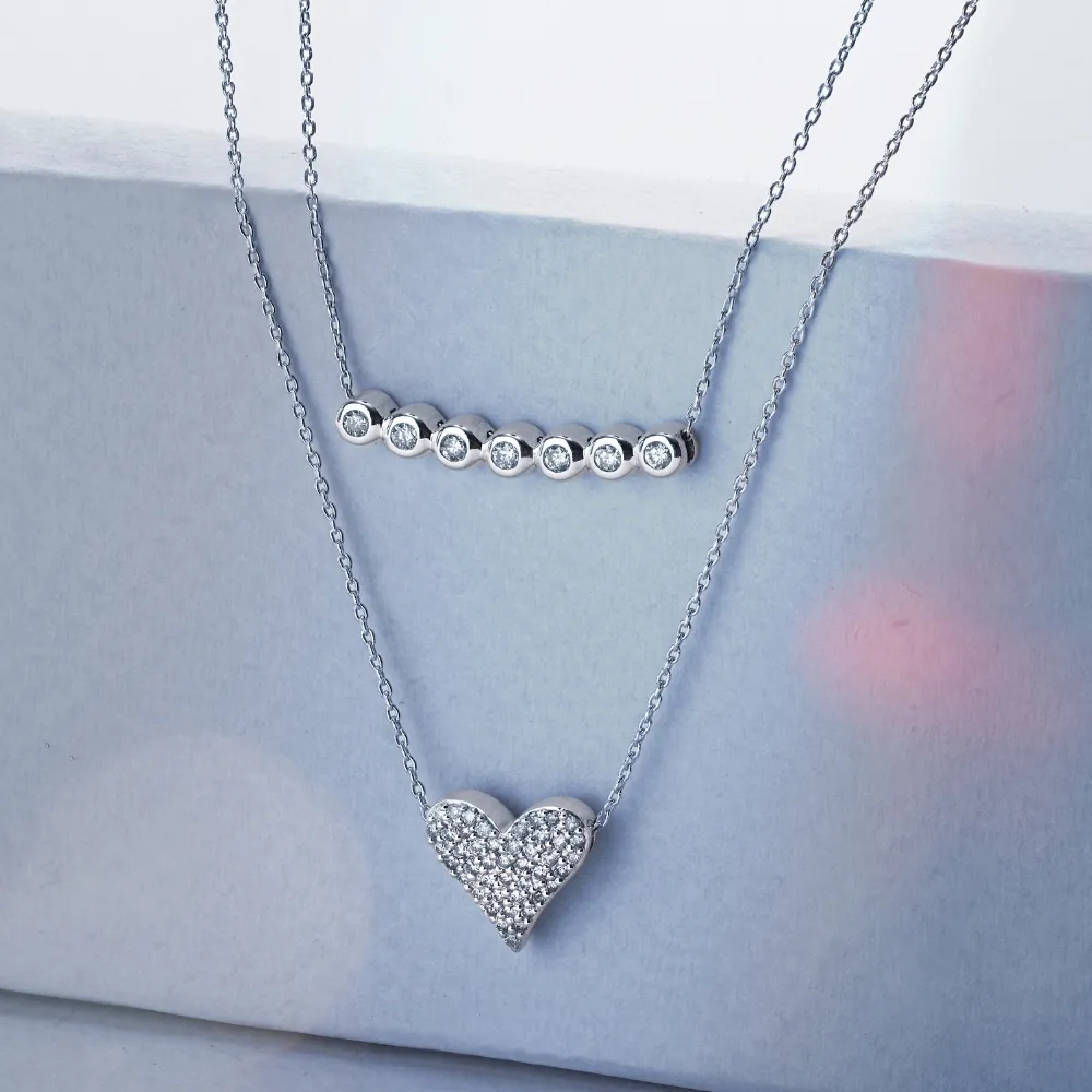Two elegant silver necklaces: one with a heart pendant and another with sparkling stones, displayed on a soft background.