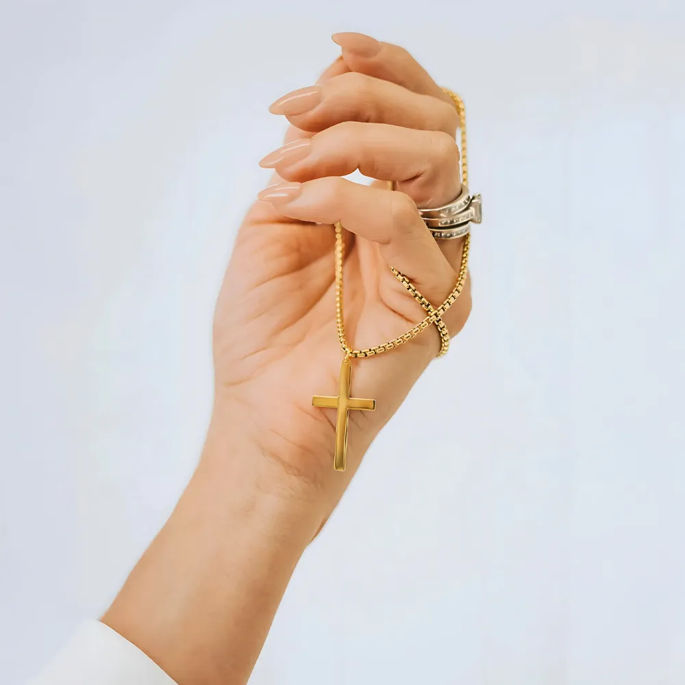 Gold cross necklace held in a hand with rings, showcasing fine jewelry.