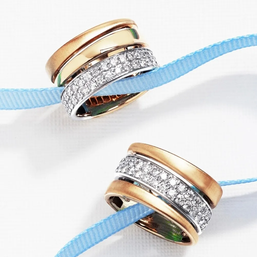 Two elegant rings with gold and silver bands, one adorned with sparkling stones, resting on a blue ribbon.