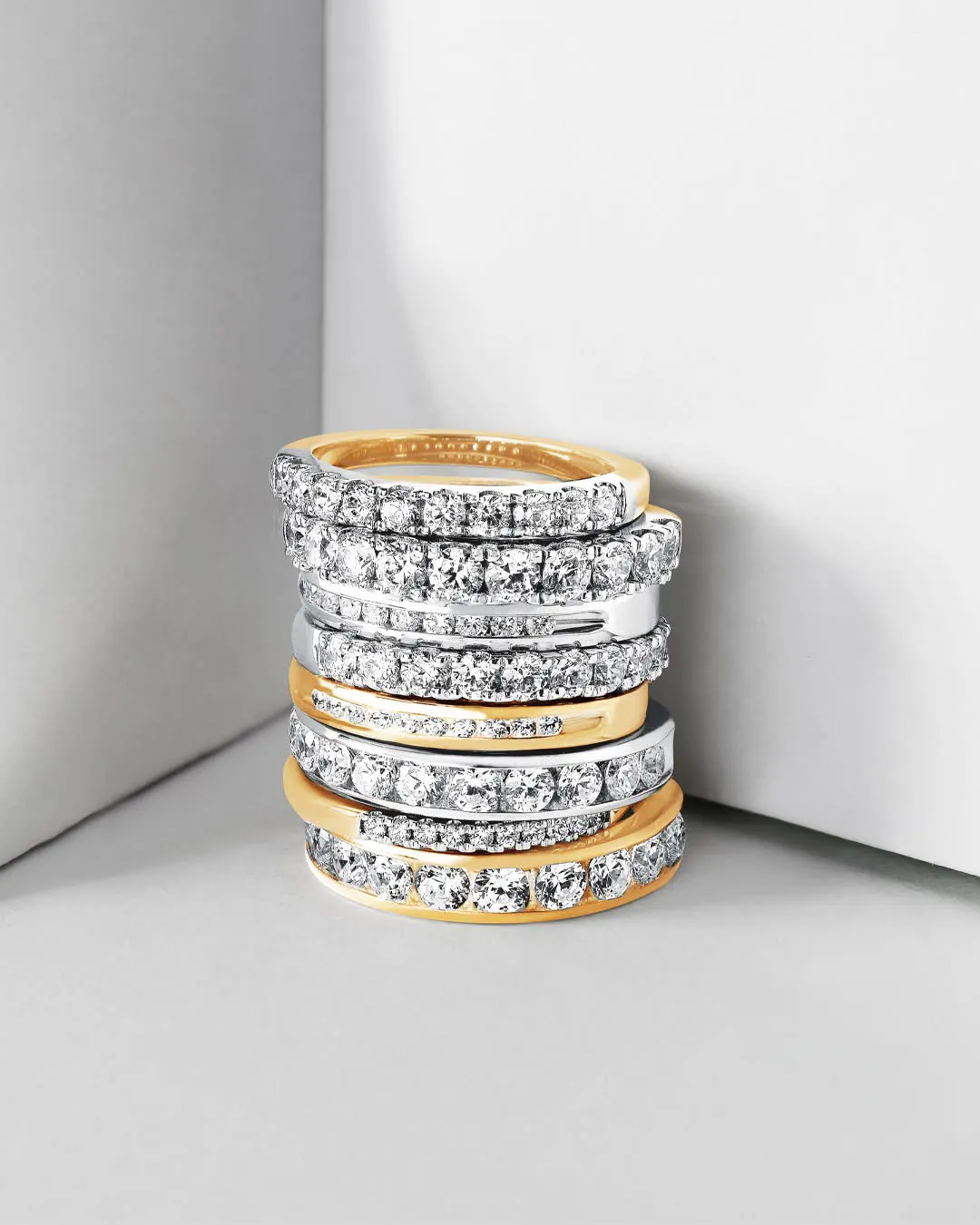 Two hands wearing intricate rings, one gold with a blue stone and one silver with colorful gems, showcasing fine jewelry.