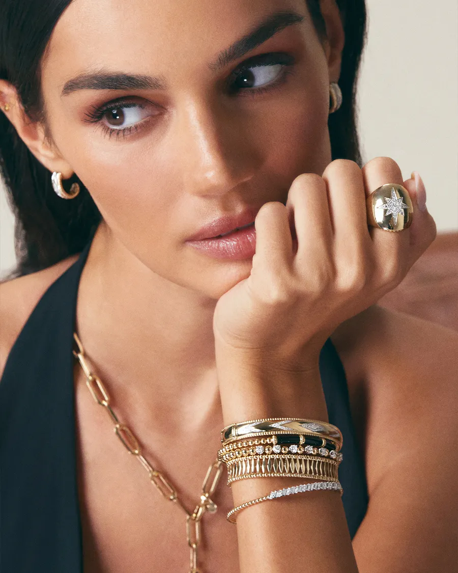 A woman showcasing gold jewelry, including a ring, bracelets, and earrings. Visit Jim Kryshak Jewelers for more.