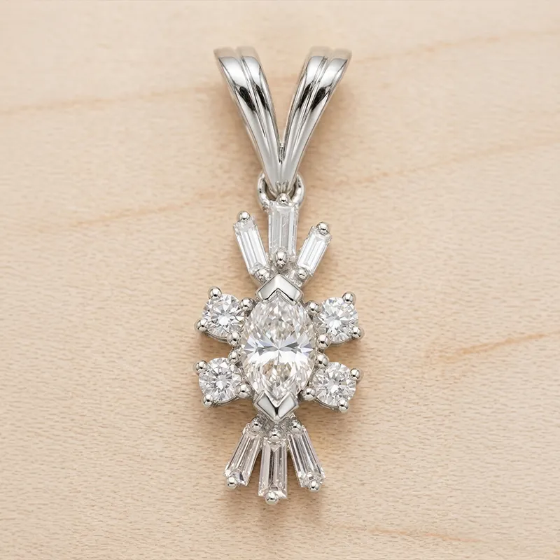 Gold pendant with a central marquise diamond, surrounded by smaller round and baguette diamonds, on a textured background.