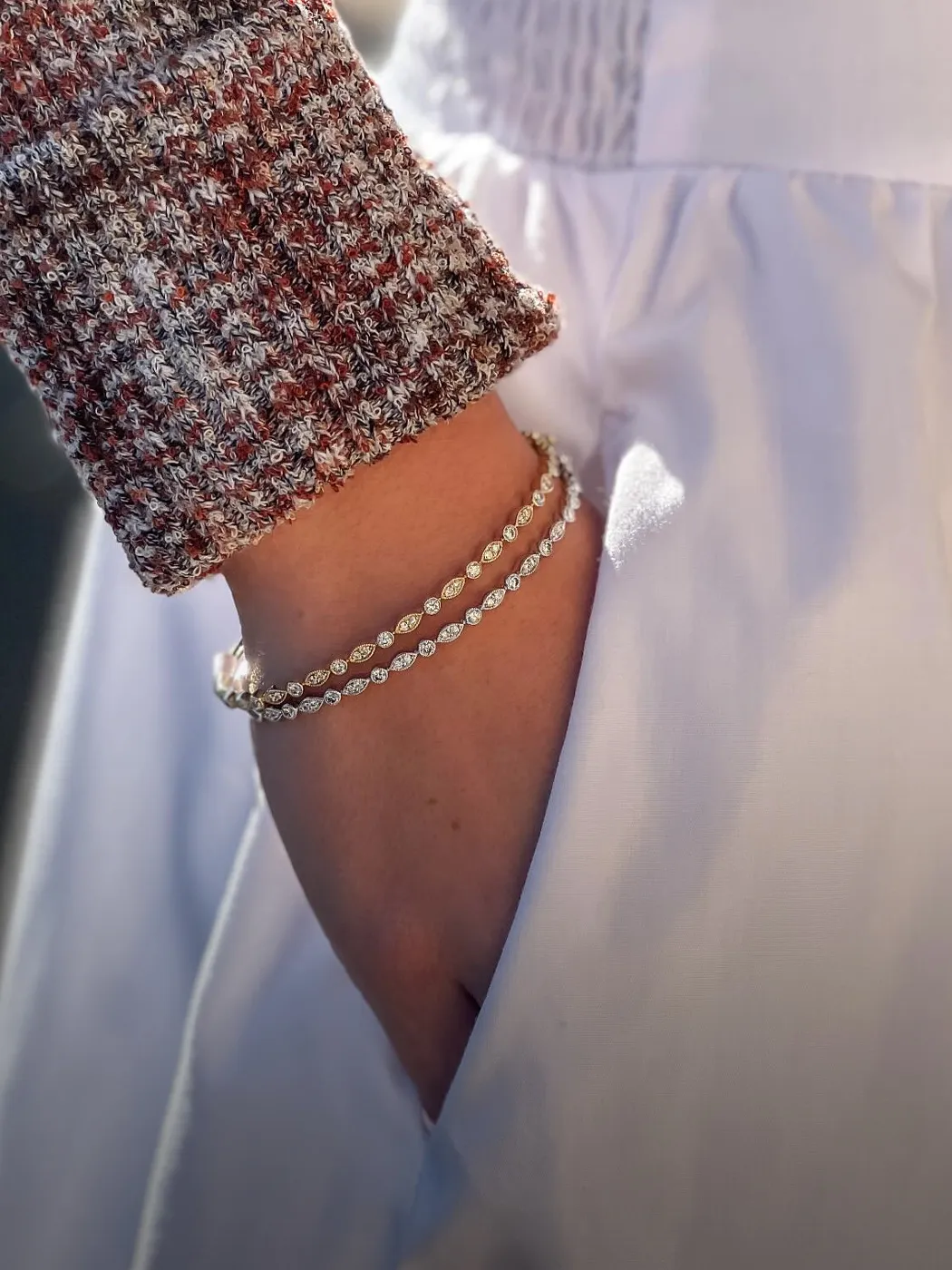 A hand with a diamond bracelet rests in a white pocket, showcasing jewelry.