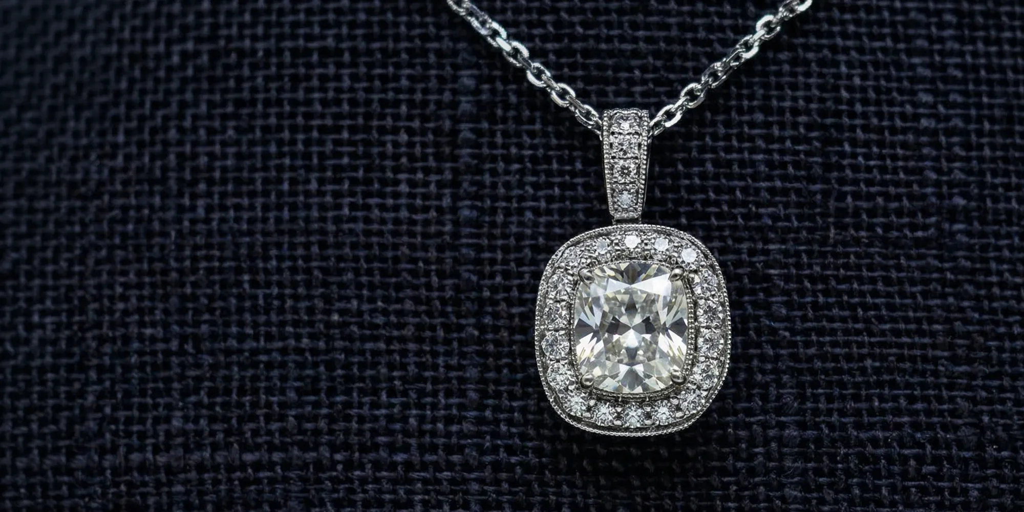 Diamond pendant necklace with halo setting on a dark textured background.