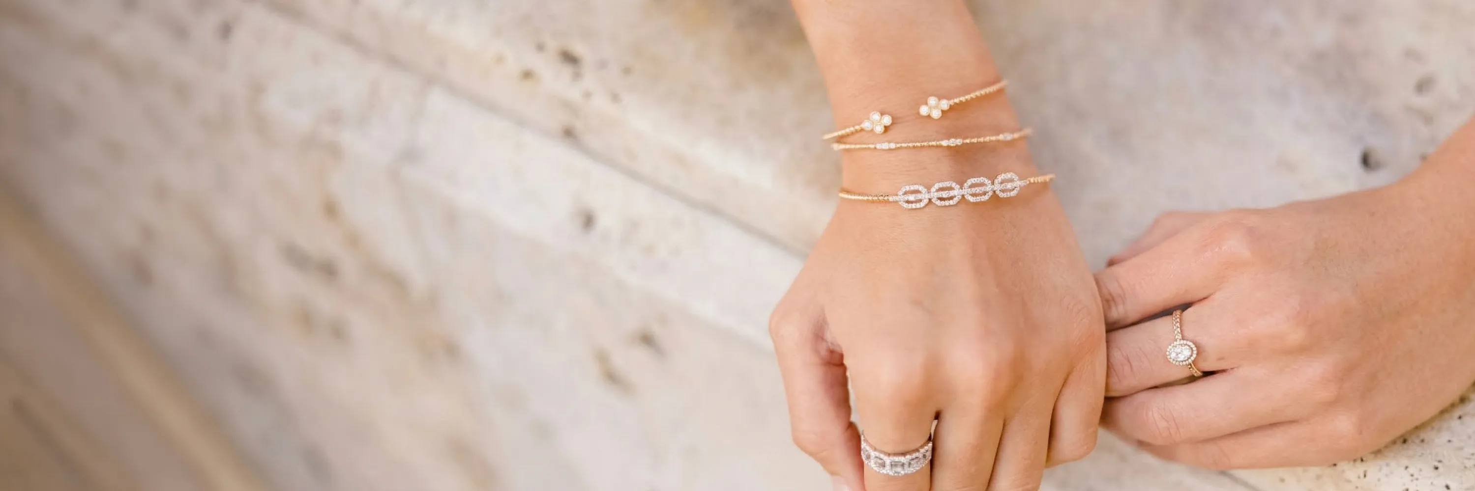 Close-up of a hand wearing elegant diamond bracelets and rings on a stone surface.
