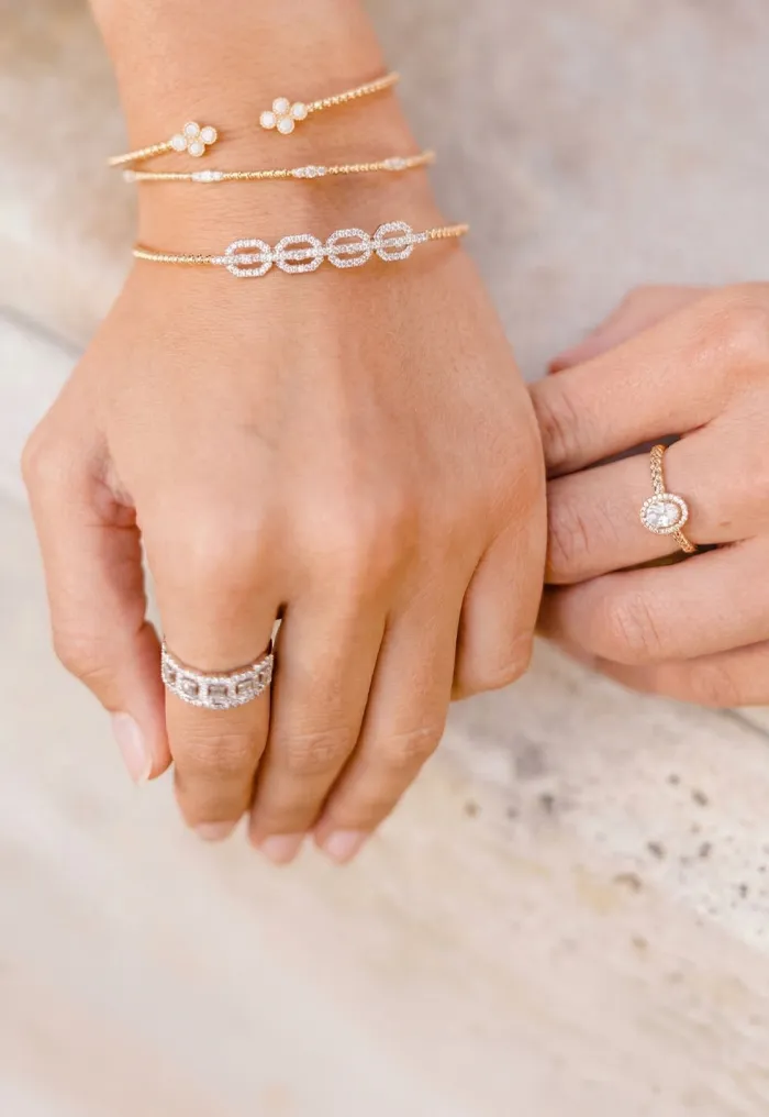 Close-up of a hand wearing elegant diamond bracelets and rings on a stone surface.