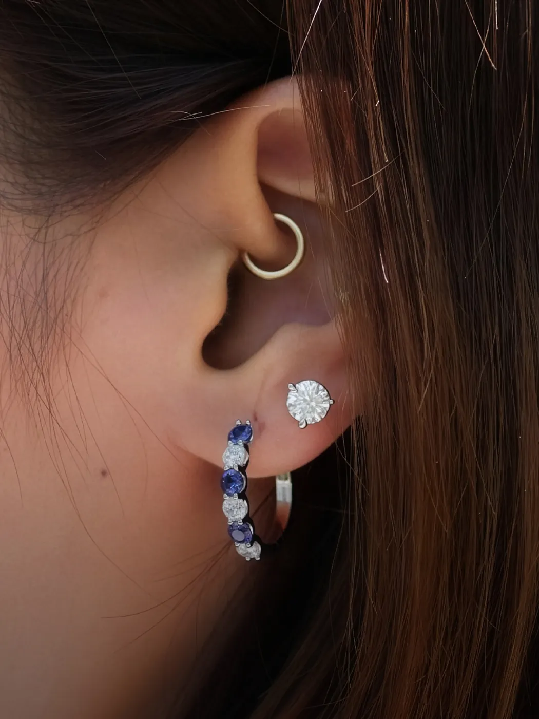 Close-up of an ear with a gold hoop and a diamond-studded earring.
