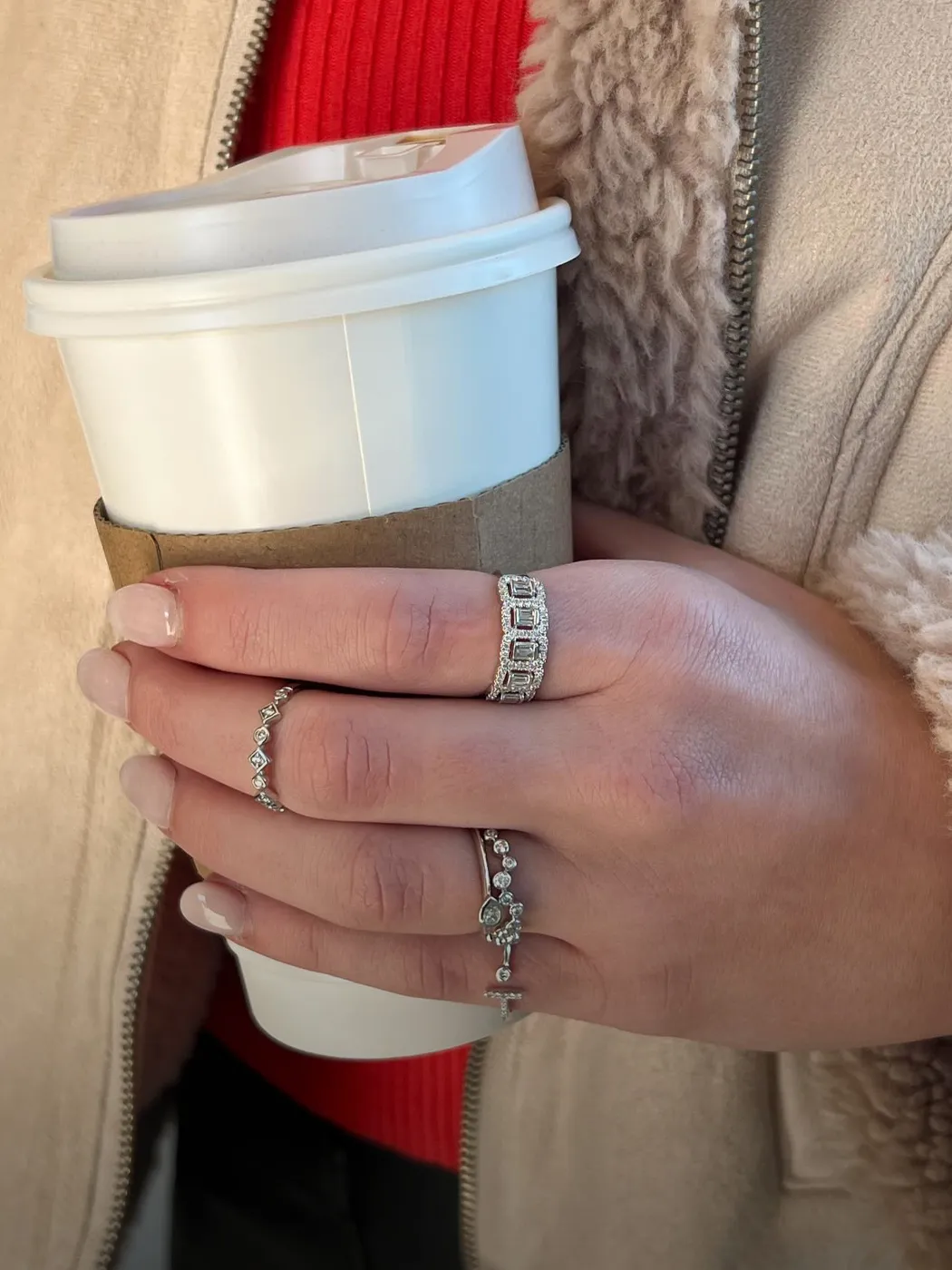 A person holding a coffee cup, showcasing multiple diamond rings on their fingers.