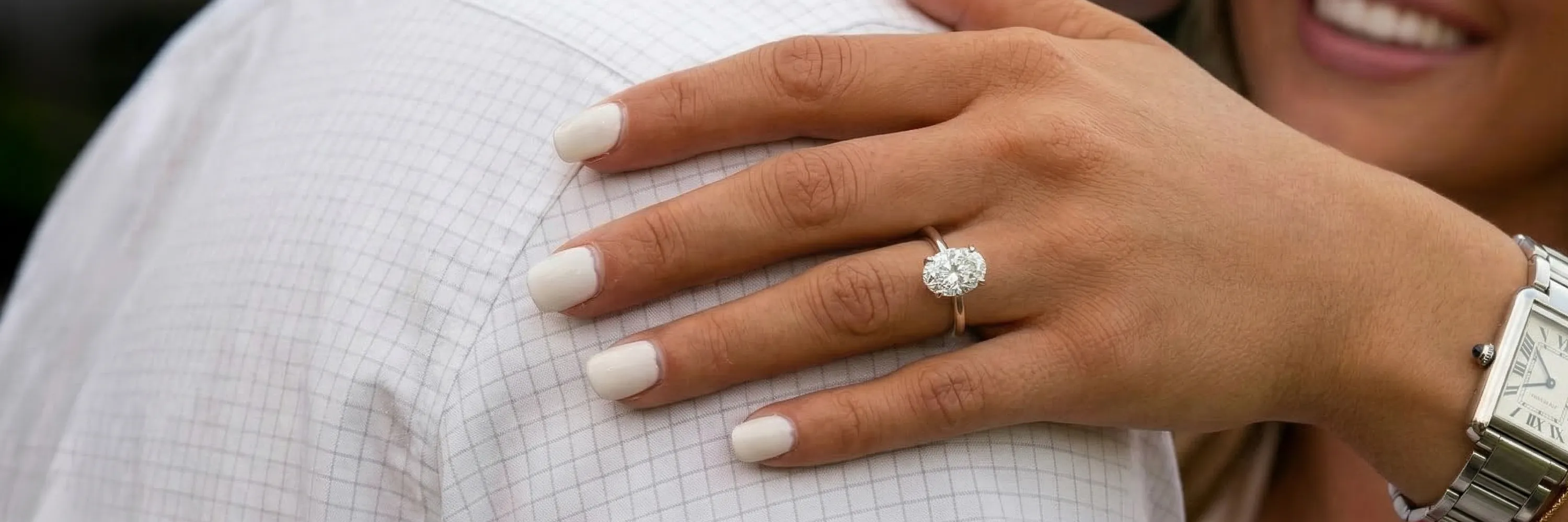 A hand with a diamond ring rests on a shoulder, showcasing an engagement ring.