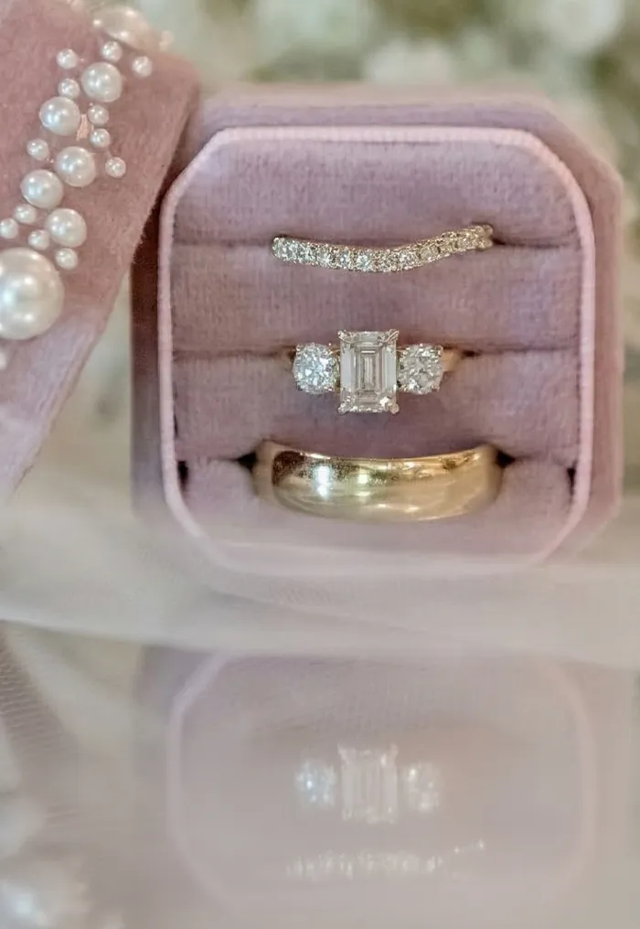 Pink velvet ring box with diamond rings and pearls, surrounded by white flowers.