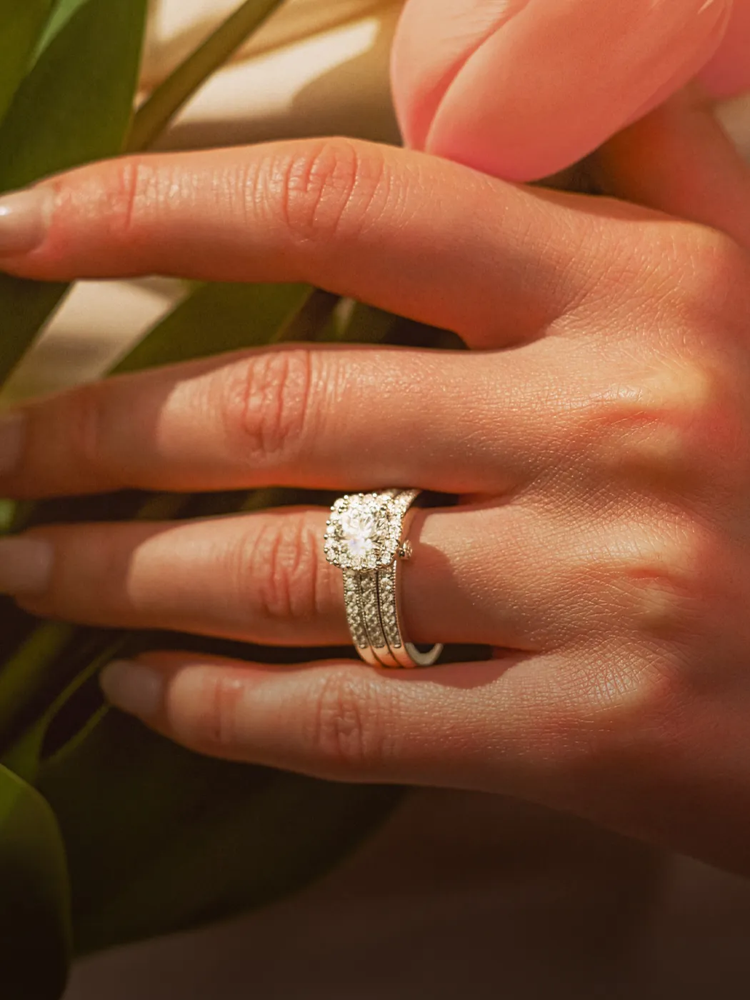 Hand with diamond engagement ring holding a pink tulip.