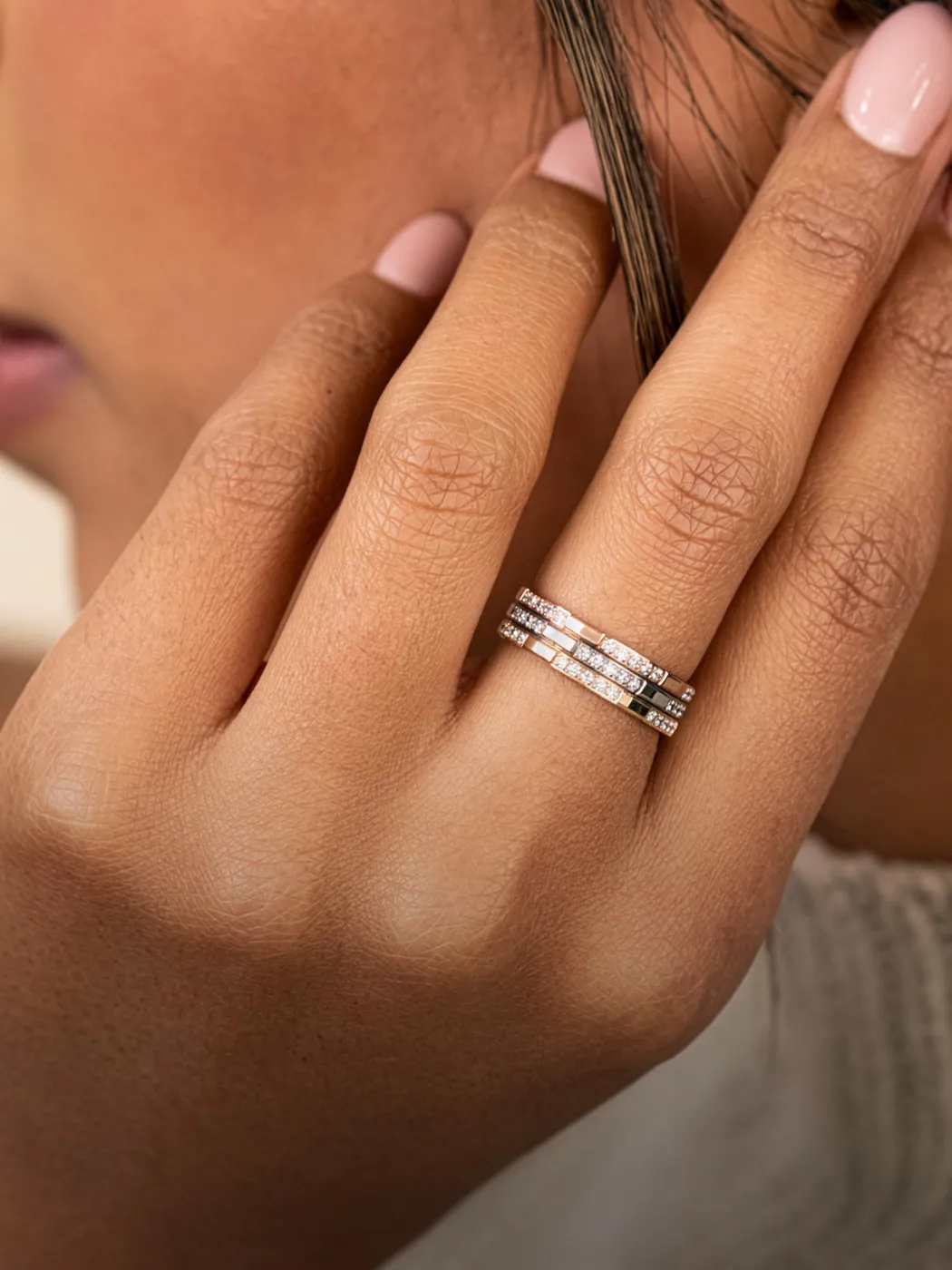 Close-up of a hand with stacked diamond rings, touching hair.