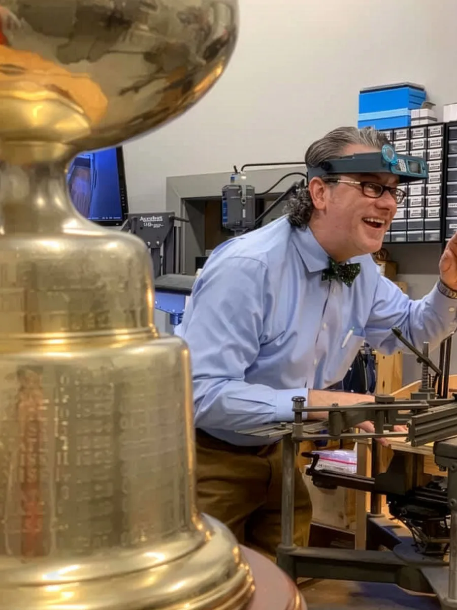 A person wearing magnifying glasses works on a large trophy in a workshop.