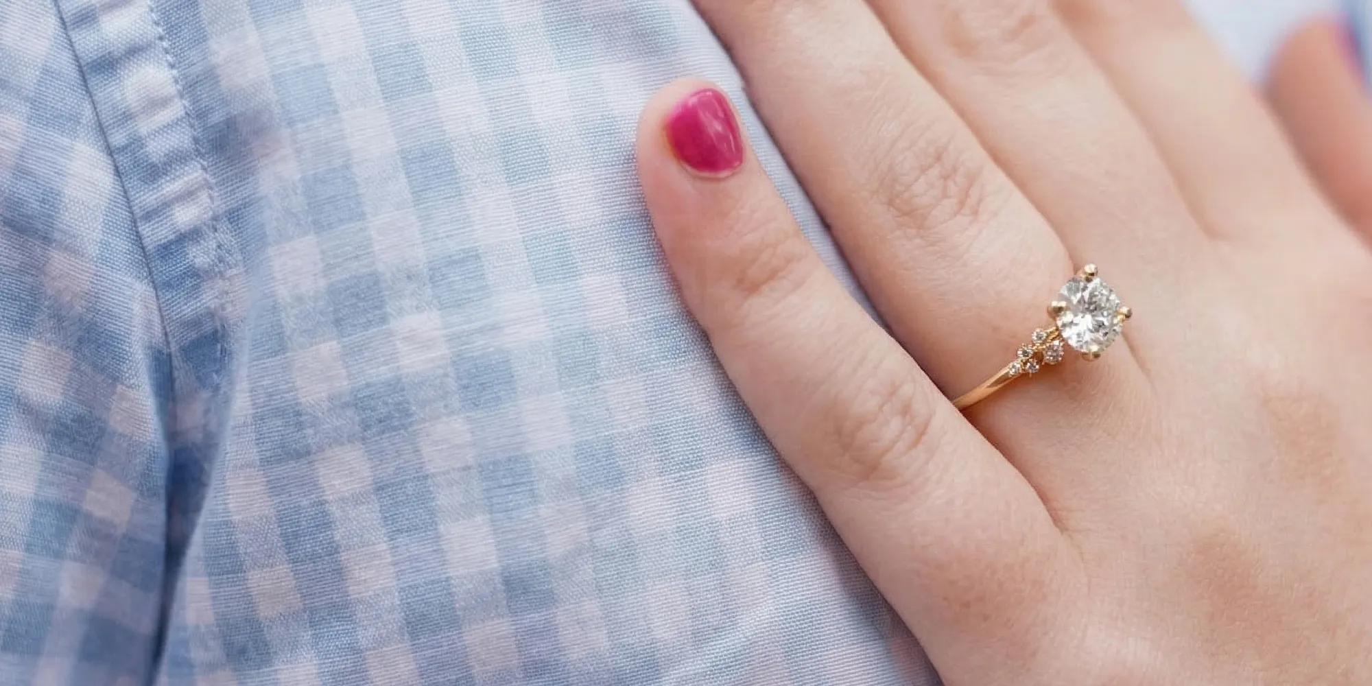 A hand with a diamond ring rests on a blue checkered fabric.